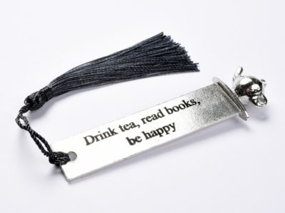 Pewter bookmark with the quotation 'Drink tea, read books, be happy' along its length. A teapot sculpture sits on top.
